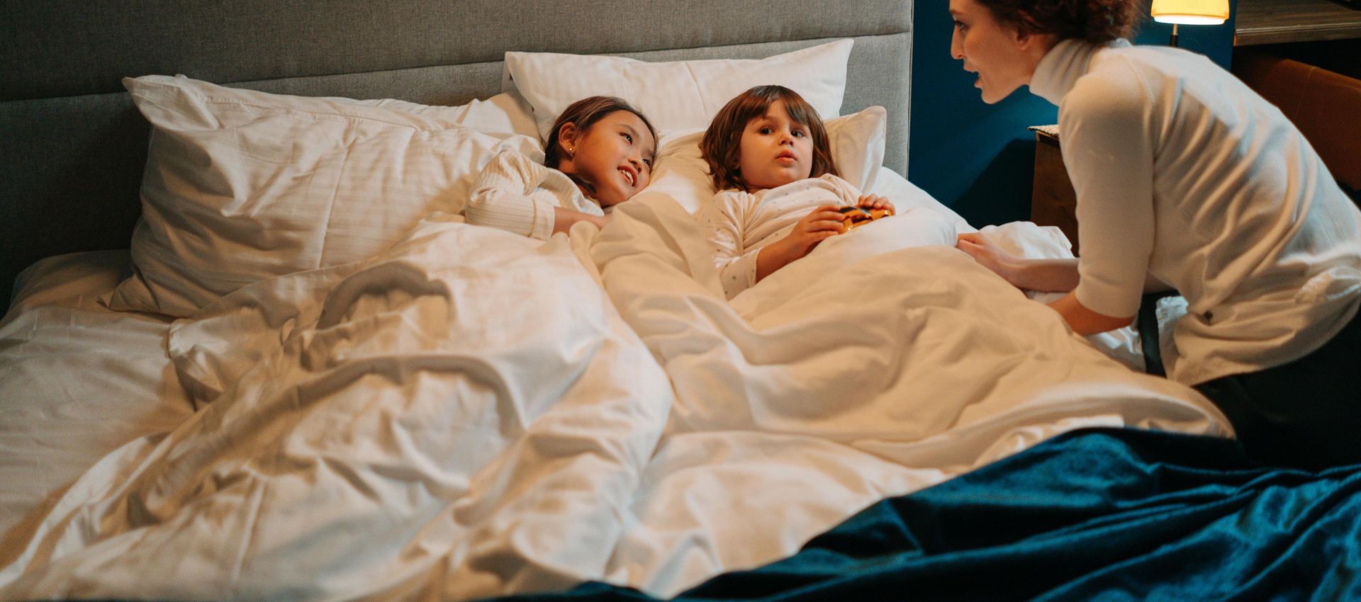 A nanny telling a bedtime story to two children in a cozy bedroom setting.
