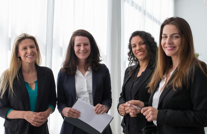 Four professional women in business attire smiling in a bright, modern office.