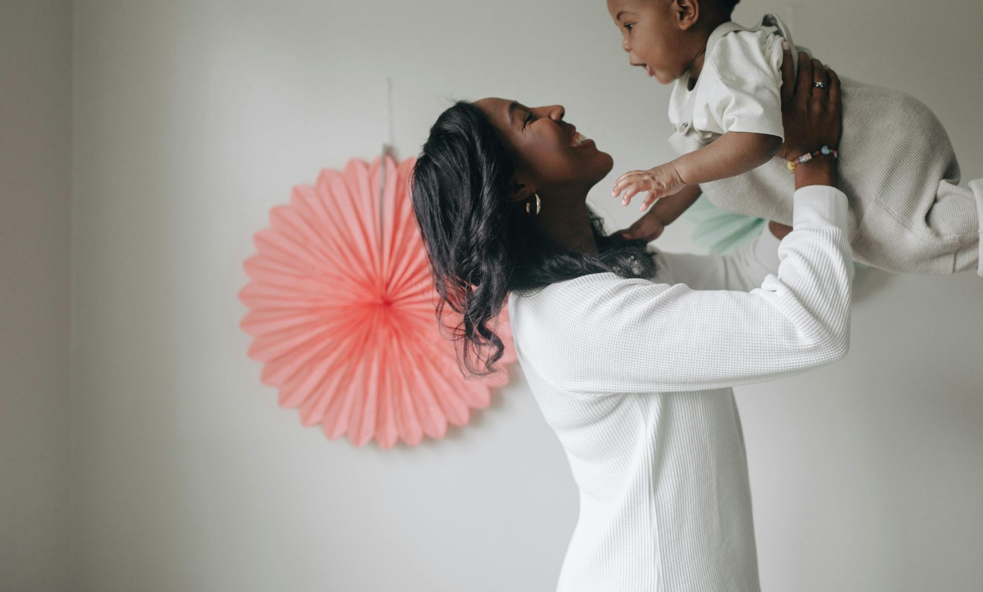 A mother lovingly lifts her baby indoors, capturing a joyful and tender moment.
