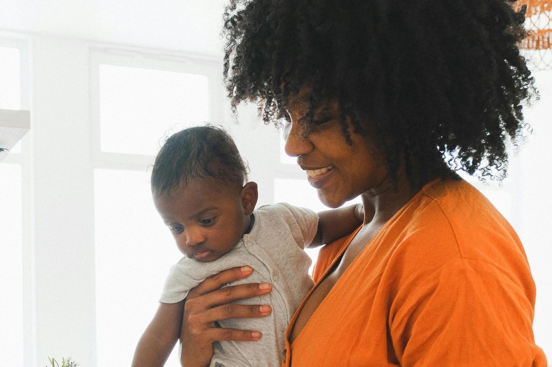A mother lovingly holds her baby in a sunny kitchen, depicting warmth and family bonding.